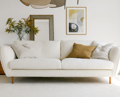 Salon moderne avec un canapé blanc, trois coussins, un tableau mural et une plante sur une table d'appoint en bois. Canape Paris by Atelier Bis