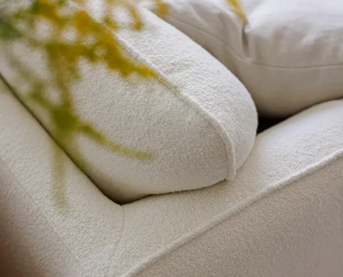 Gros plan d'un canapé texturé de couleur crème avec une plante jaune-vert floue au premier plan. Canape Paris by Atelier Bis