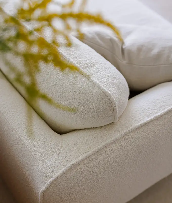 Gros plan d'un canapé texturé de couleur crème avec une plante jaune-vert floue au premier plan. Canape Paris by Atelier Bis