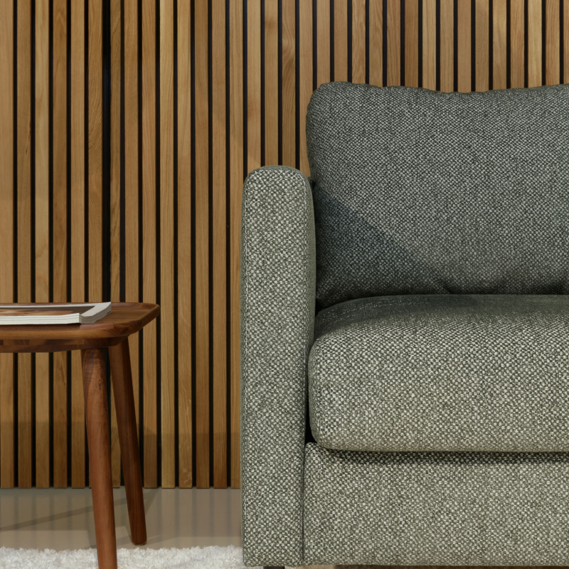 Canapé gris et table d'appoint en bois sur tapis blanc, contre un mur vertical en lattes de bois. Canape Paris by Atelier Bis