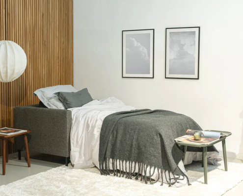 Un lit bien fait avec une literie grise, une table d'appoint et un tableau mural dans une chambre à coucher moderne et minimaliste. Canape Paris by Atelier Bis