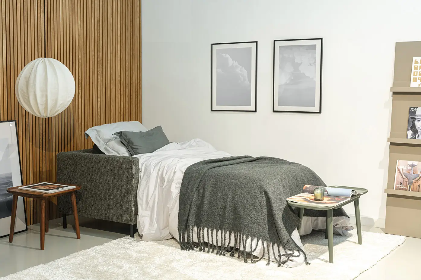 Un lit bien fait avec une literie grise, une table d'appoint et un tableau mural dans une chambre à coucher moderne et minimaliste. Canape Paris by Atelier Bis