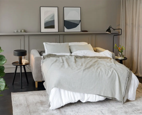 Une chambre à coucher confortable avec un lit moderne, une literie grise, des œuvres d'art murales, des plantes et un éclairage naturel doux. Canape Paris by Atelier Bis