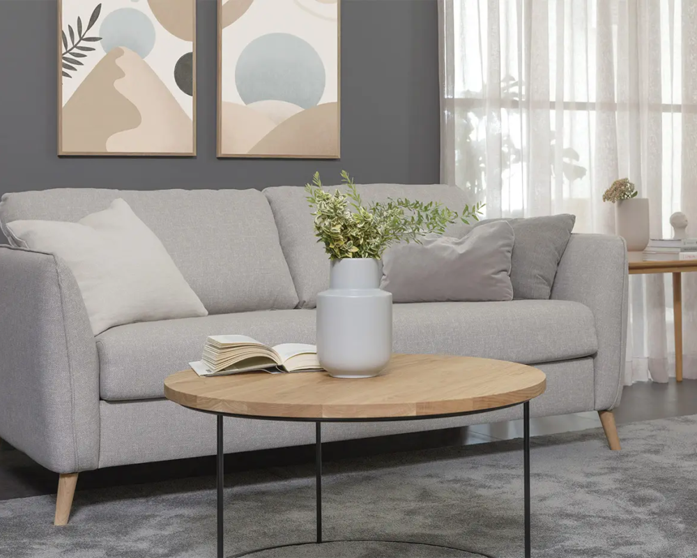 Salon moderne avec un canapé gris, une table basse ronde en bois et une décoration minimaliste. Canape Paris by Atelier Bis