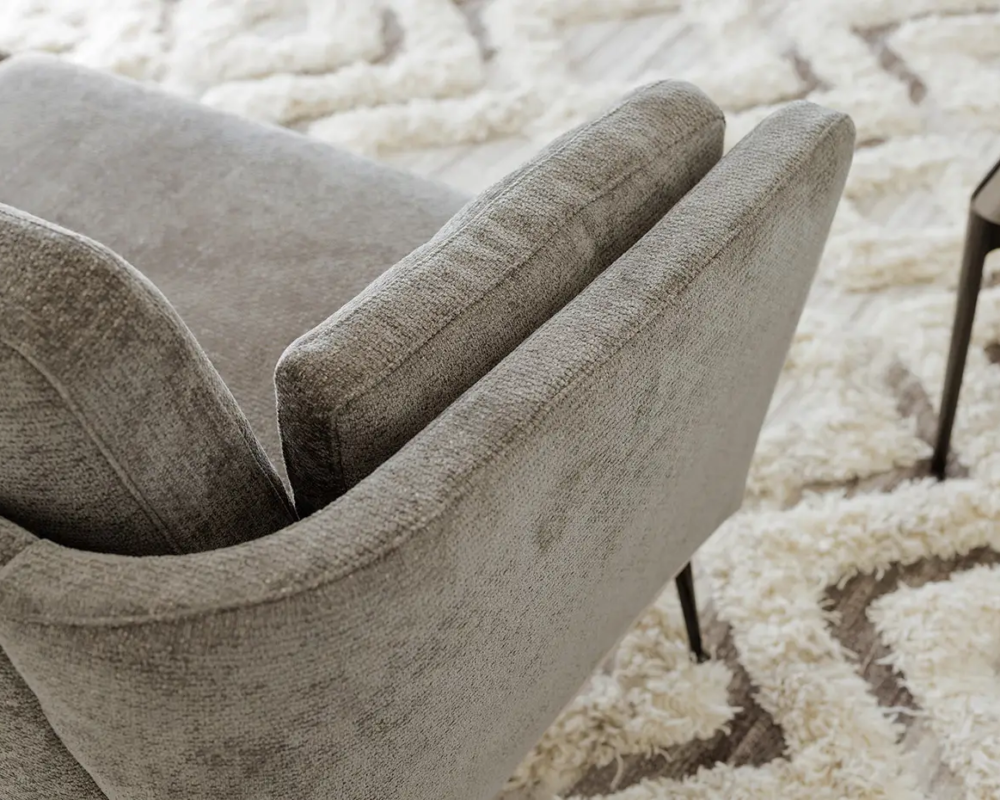 Fauteuil gris rembourré sur un tapis texturé crème et beige avec une petite plante sur une table d'appoint à proximité. Canape Paris by Atelier Bis