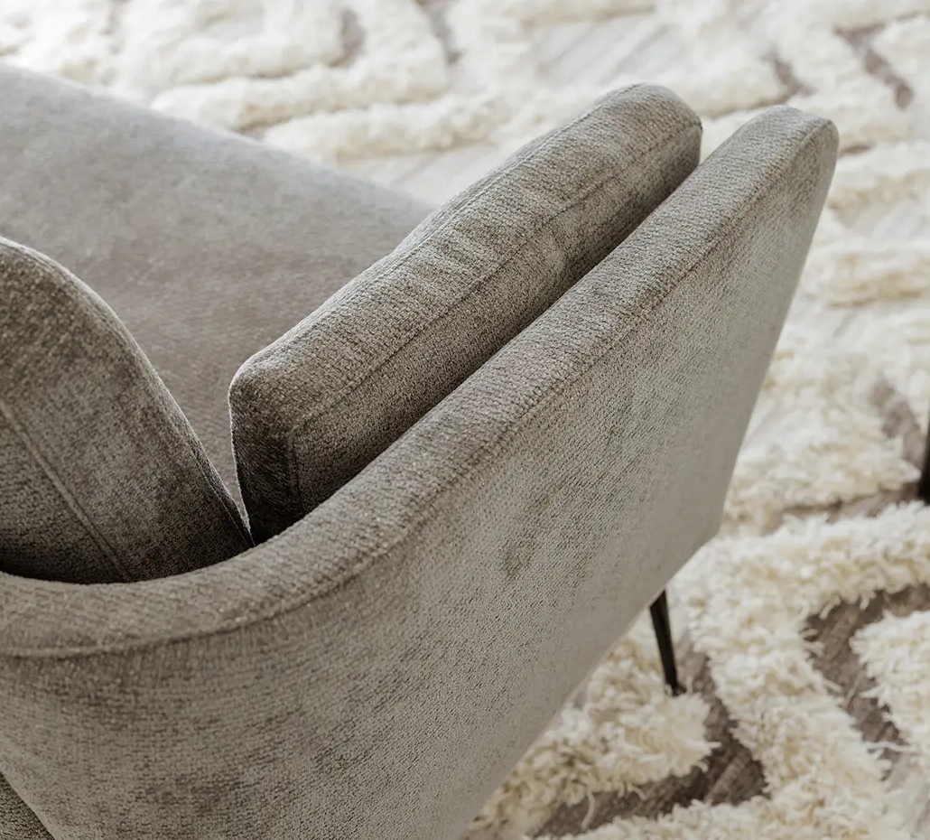 Fauteuil gris rembourré sur un tapis texturé crème et beige avec une petite plante sur une table d'appoint à proximité. Canape Paris by Atelier Bis