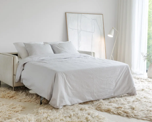 Chambre à coucher lumineuse avec un canapé-lit blanc, un tapis moelleux, un lampadaire et des œuvres d'art abstraites contre le mur. Canape Paris by Atelier Bis