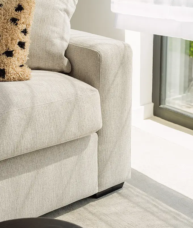 Gros plan sur un canapé gris clair avec un oreiller près d'une fenêtre ensoleillée et d'un rideau blanc transparent. Canape Paris by Atelier Bis