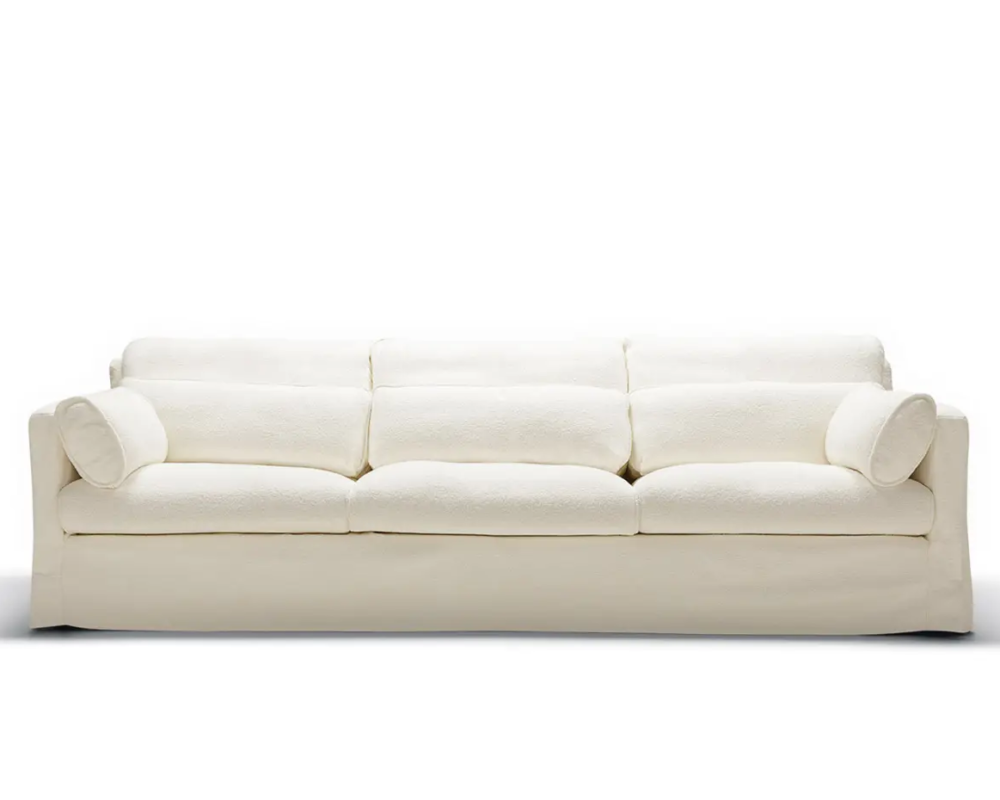 Canapé blanc à trois places avec des coussins en peluche et deux coussins cylindriques, sur fond blanc. Canape Paris by Atelier Bis