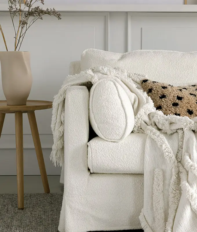 Fauteuil blanc douillet avec un jeté gommé, un oreiller texturé et un vase sur une table d'appoint en bois. Canape Paris by Atelier Bis