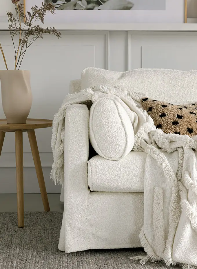 Fauteuil blanc douillet avec un jeté gommé, un oreiller texturé et un vase sur une table d'appoint en bois. Canape Paris by Atelier Bis