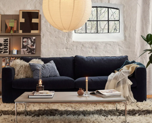 Salon confortable avec canapé sombre, table basse, bougies, livres, œuvres d'art sur des étagères et une grande lampe ronde en papier. Canape Paris by Atelier Bis