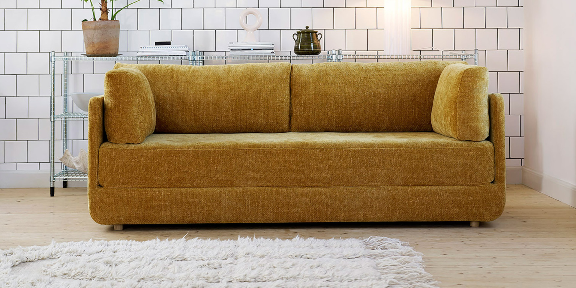 Canapé jaune moutarde avec coussins dans une pièce moderne avec des murs carrelés et un tapis blanc sur un sol en bois. Canape Paris by Atelier Bis