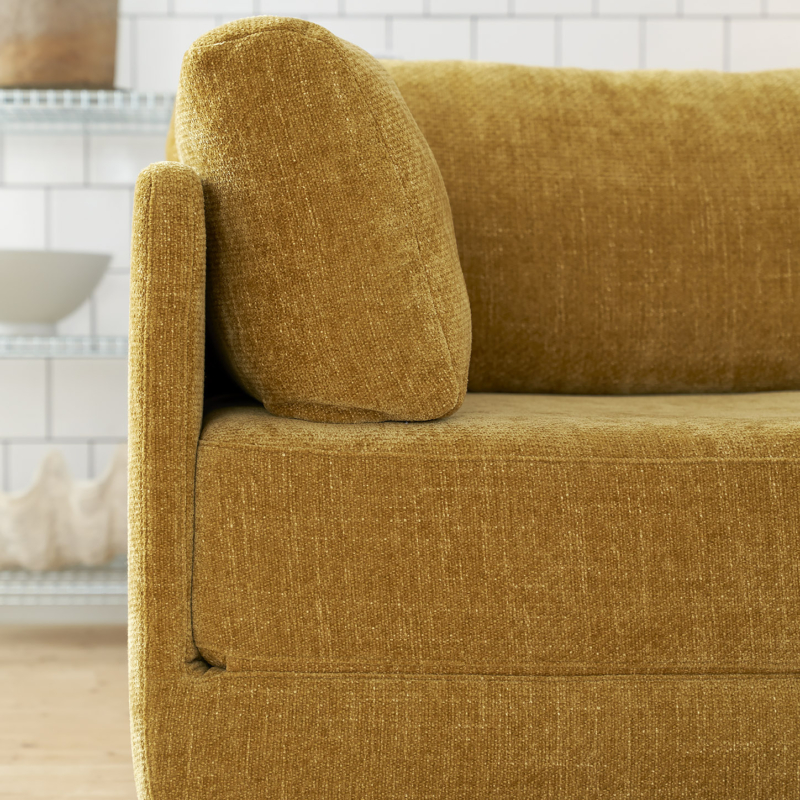 Gros plan sur un canapé jaune moutarde au tissu texturé dans un salon moderne au mur carrelé blanc. Canape Paris by Atelier Bis