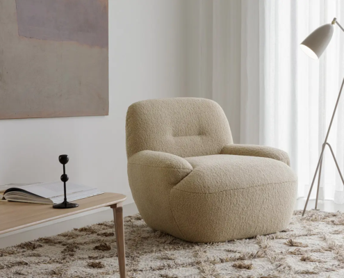 Fauteuil beige sur un tapis texturé à côté d'un lampadaire et d'une table basse dans une pièce à l'éclairage tamisé. Canape Paris by Atelier Bis