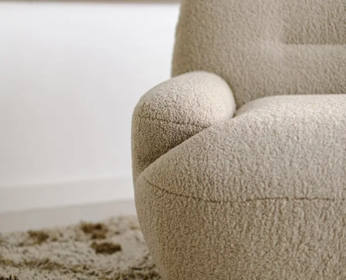 Gros plan sur un fauteuil beige et texturé posé sur un tapis shaggy dans une pièce minimaliste. Canape Paris by Atelier Bis
