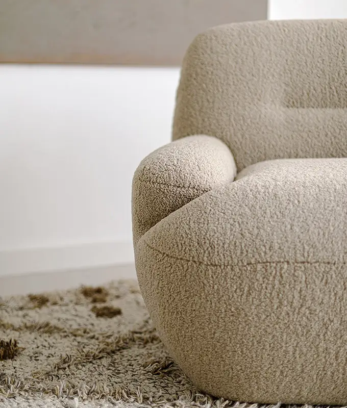 Gros plan sur un fauteuil beige et texturé posé sur un tapis shaggy dans une pièce minimaliste. Canape Paris by Atelier Bis