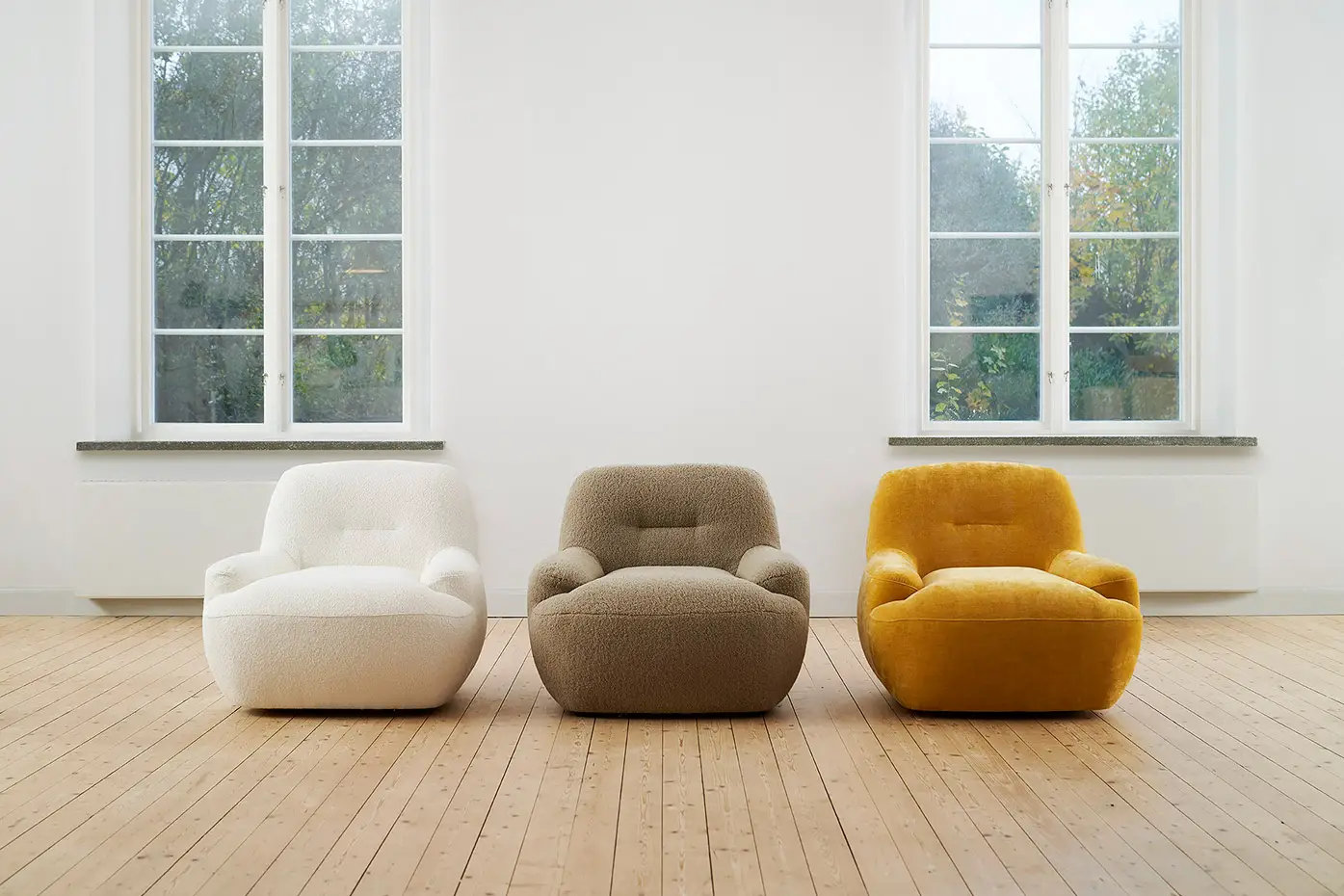 Trois fauteuils modernes - blanc, gris et jaune - sont posés côte à côte dans une pièce lumineuse au sol en bois. Canape Paris by Atelier Bis