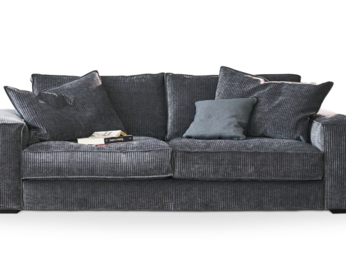 Canapé en velours côtelé gris foncé avec quatre coussins, un livre et des lunettes posés sur le siège de gauche. Canape Paris by Atelier Bis