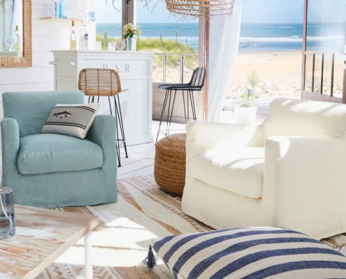 Salon confortable en bord de mer avec deux fauteuils, un bar et une vue sur l'océan à travers des portes vitrées ouvertes. Canape Paris by Atelier Bis