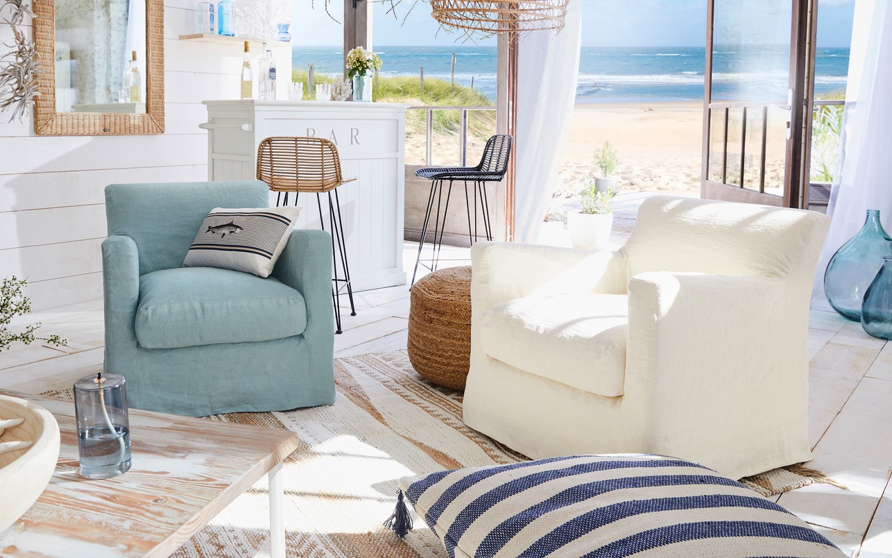 Salon confortable en bord de mer avec deux fauteuils, un bar et une vue sur l'océan à travers des portes vitrées ouvertes. Canape Paris by Atelier Bis