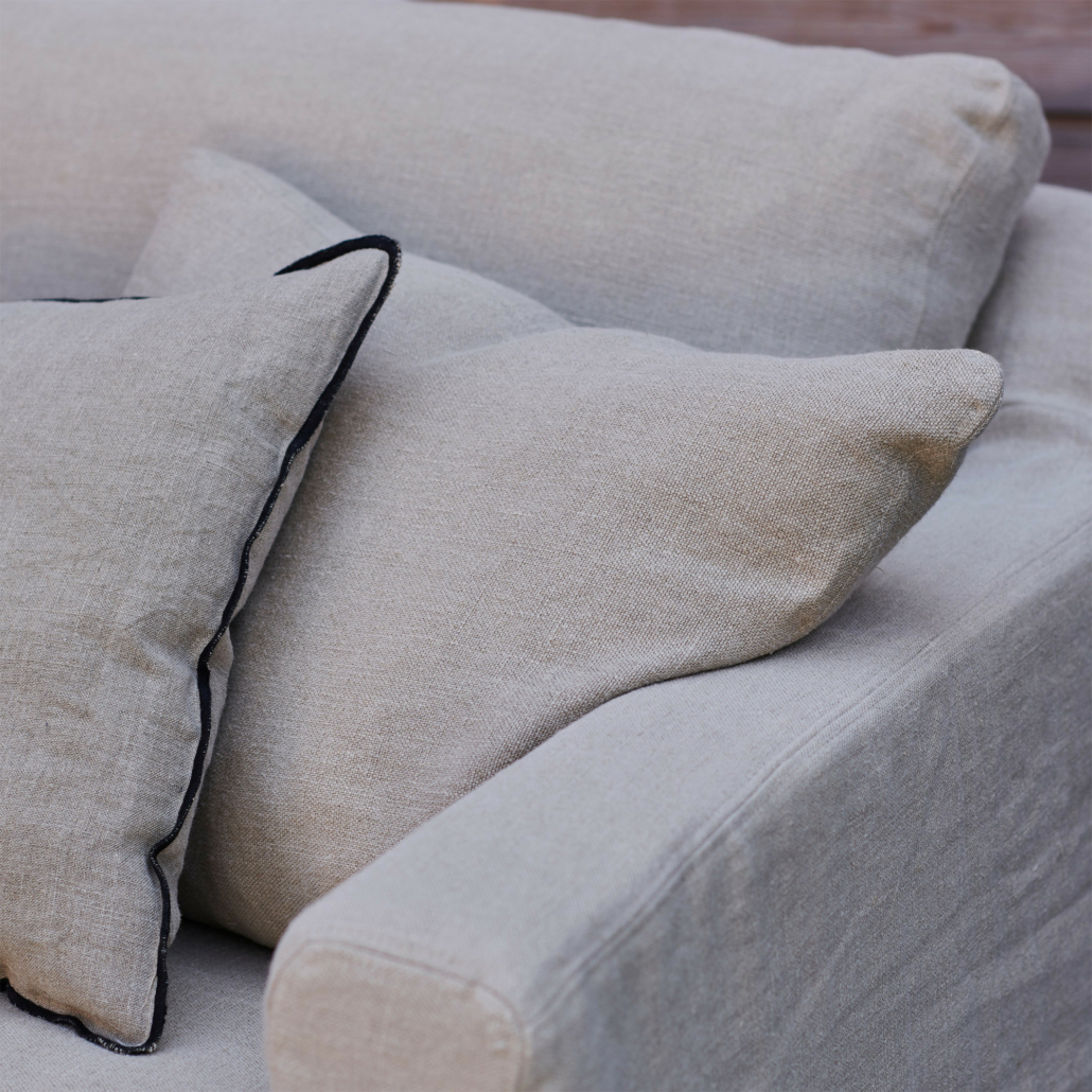 Gros plan sur un canapé beige avec deux coussins, dont l'un est orné d'une bordure sombre. Canape Paris by Atelier Bis