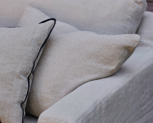 Gros plan sur un canapé beige avec deux coussins, dont l'un est orné d'une bordure sombre. Canape Paris by Atelier Bis