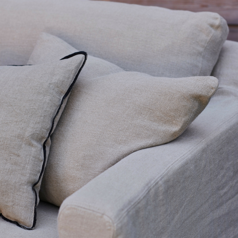 Gros plan sur un canapé beige avec deux coussins, dont l'un est orné d'une bordure sombre. Canape Paris by Atelier Bis