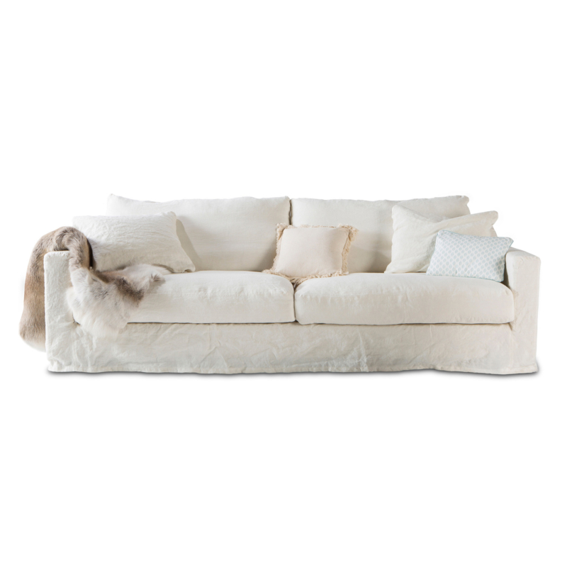 Canapé blanc avec quatre coussins et un jeté de fourrure drapé sur un bras, sur fond blanc. Canape Paris by Atelier Bis