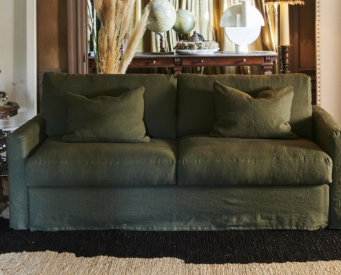 Canapé vert avec deux coussins assortis dans un salon élégant et confortable à la décoration éclectique et à l'éclairage chaleureux. Canape Paris by Atelier Bis