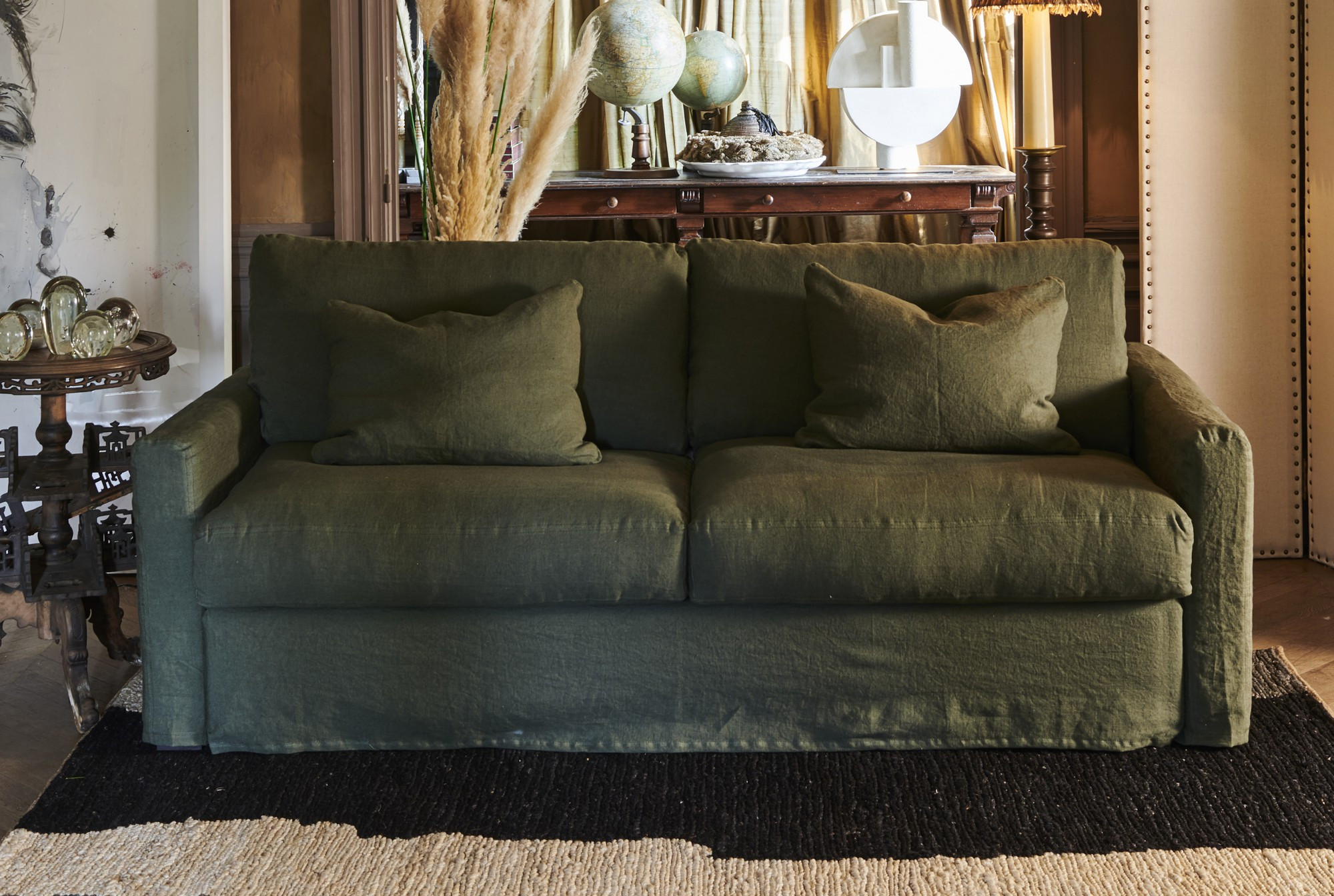 Canapé vert avec deux coussins assortis dans un salon élégant et confortable à la décoration éclectique et à l'éclairage chaleureux. Canape Paris by Atelier Bis