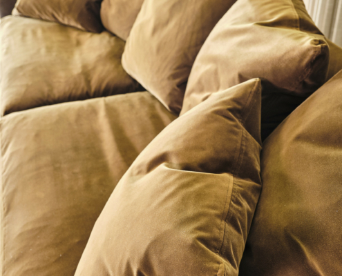 Un canapé en velours marron avec des coussins en peluche assortis, placé près d'une fenêtre avec de la verdure à l'extérieur. Canape Paris by Atelier Bis