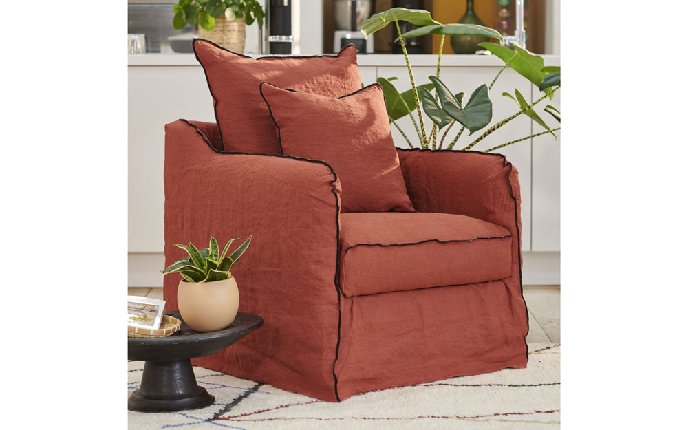 Un fauteuil couleur rouille avec deux coussins assortis à côté de plantes d'intérieur vertes dans un salon confortable. Canape Paris by Atelier Bis