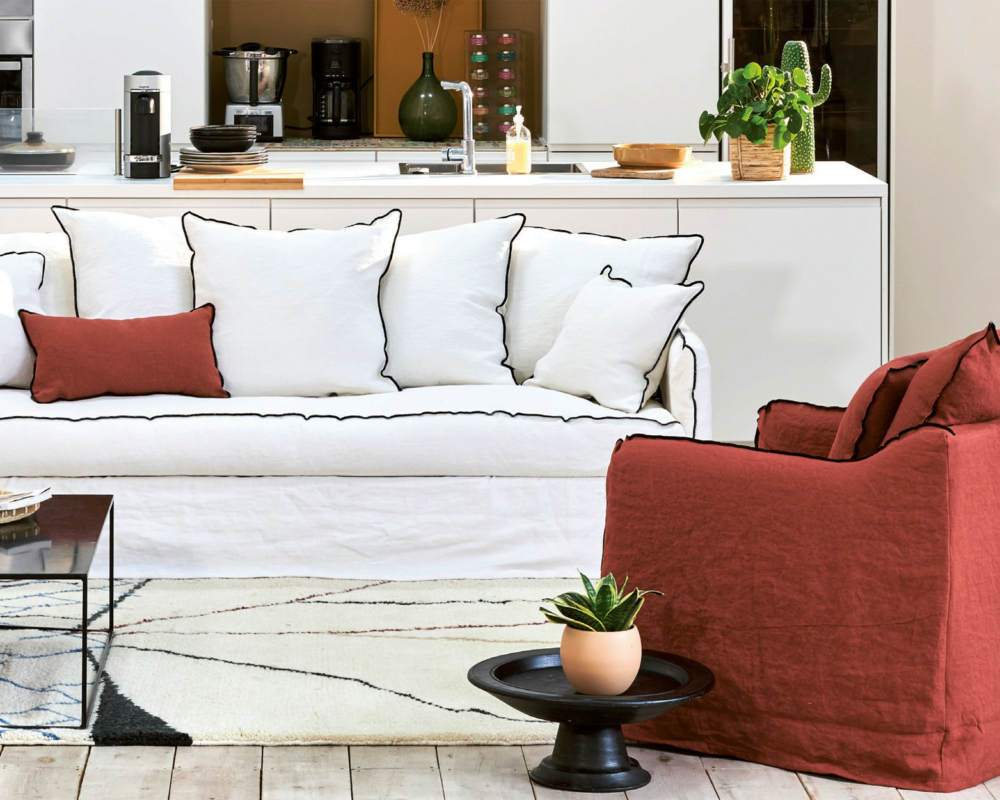 Canapé blanc convertible Homespirit avec des coussins blancs, un coussin rouge et un fauteuil rouge dans un salon moderne avec des plantes - parfait pour ajouter une touche Cassis. Canape Paris by Atelier Bis