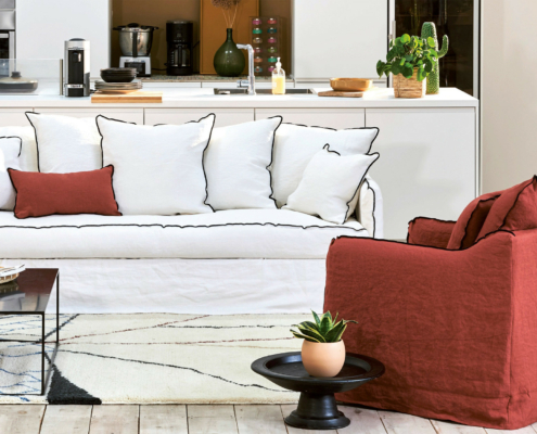 Canapé blanc convertible Homespirit avec des coussins blancs, un coussin rouge et un fauteuil rouge dans un salon moderne avec des plantes - parfait pour ajouter une touche Cassis. Canape Paris by Atelier Bis
