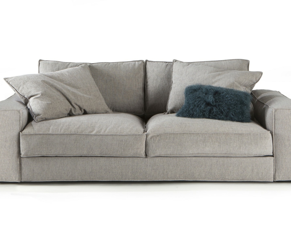 Canapé gris clair avec deux grands coussins et un coussin en fourrure gris foncé sur fond blanc. Canape Paris by Atelier Bis