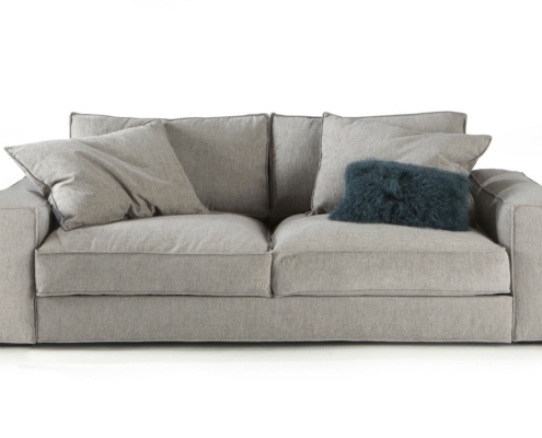 Canapé gris clair avec deux grands coussins et un coussin en fourrure gris foncé sur fond blanc. Canape Paris by Atelier Bis