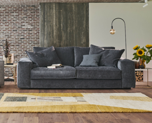 Canapé gris foncé avec coussins, tapis, tournesols et lampadaire dans un salon moderne. Canape Paris by Atelier Bis