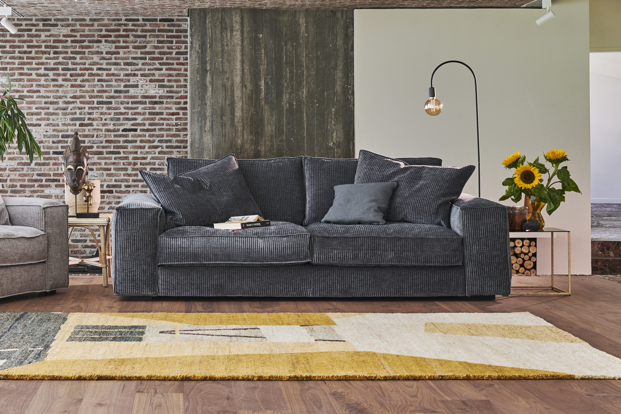 Canapé gris foncé avec coussins, tapis, tournesols et lampadaire dans un salon moderne. Canape Paris by Atelier Bis