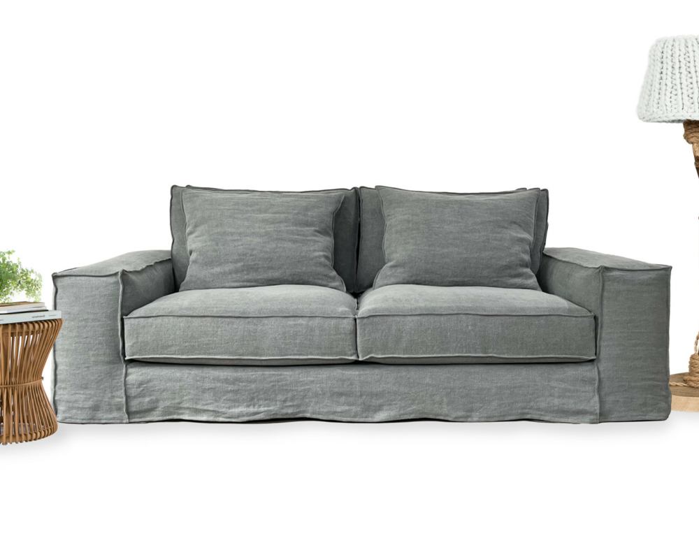 Un canapé gris avec une lampe en tricot à droite et une table d'appoint en osier avec une plante et des livres à gauche. Canape Paris by Atelier Bis