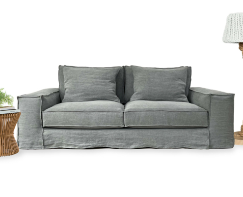 Un canapé gris avec une lampe en tricot à droite et une table d'appoint en osier avec une plante et des livres à gauche. Canape Paris by Atelier Bis