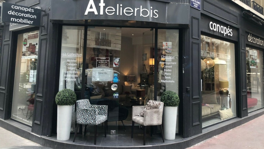 Un magasin de meubles et de décoration avec de grandes fenêtres, des chaises modernes et des plantes en pot à l'entrée. Canape Paris by Atelier Bis