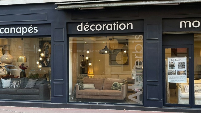 Devanture de magasin avec de grandes vitrines présentant des canapés et des objets de décoration ; les enseignes indiquent "canapés", "décoration", "mobilier". Canape Paris by Atelier Bis