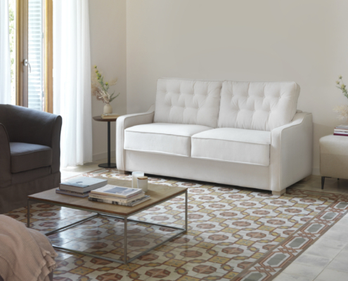 Salon lumineux avec un canapé convertible PAMPELUNE, un sol carrelé à motifs, une table basse et la lumière du soleil à travers des rideaux transparents. Canape Paris by Atelier Bis