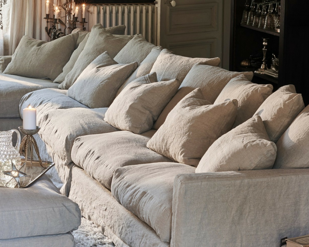 Le canapé beige Homesprit Biscarrosse déhoussable avec de nombreux coussins, un plateau éclairé à la bougie et un tapis moelleux créent un salon confortable et élégant. Canape Paris by Atelier Bis