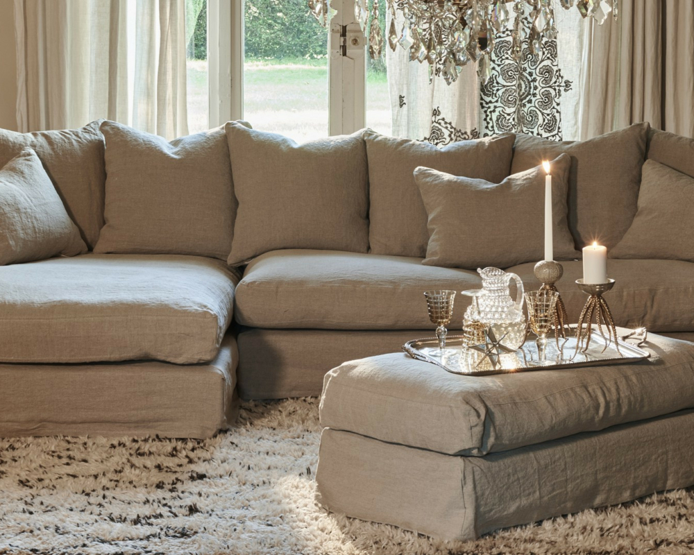 Canapé confortable Homesprit Biscarrosse déhoussable avec coussins et pouf, bougies et verres sur un plateau dans un salon chaleureusement éclairé. Canape Paris by Atelier Bis