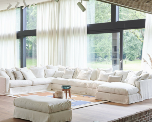 canape-3-places-biarritz-206-cm Salon spacieux avec un grand canapé Homesprit Biscarrosse déhoussable, un ottoman et des fenêtres allant du sol au plafond avec des rideaux diaphanes. Canape Paris by Atelier Bis
