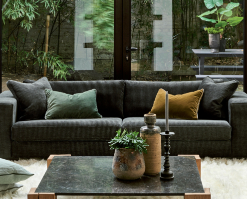 vang 2 Canapé gris foncé avec coussins verts et moutarde, table basse, plantes et portes vitrées ouvrant sur un jardin. Canape Paris by Atelier Bis